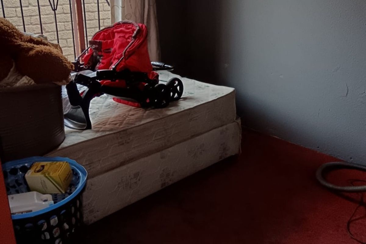 A bedroom featuring carpeted flooring and a window with a security gate, currently requiring cosmetic updates and maintenance.