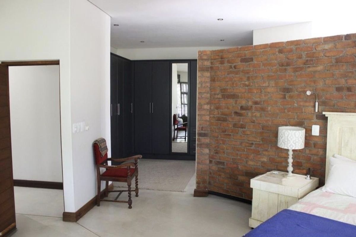 Spacious bedroom featuring a modern exposed brick partition wall, polished concrete floors, and extensive built-in cabinetry with a mirrored panel.