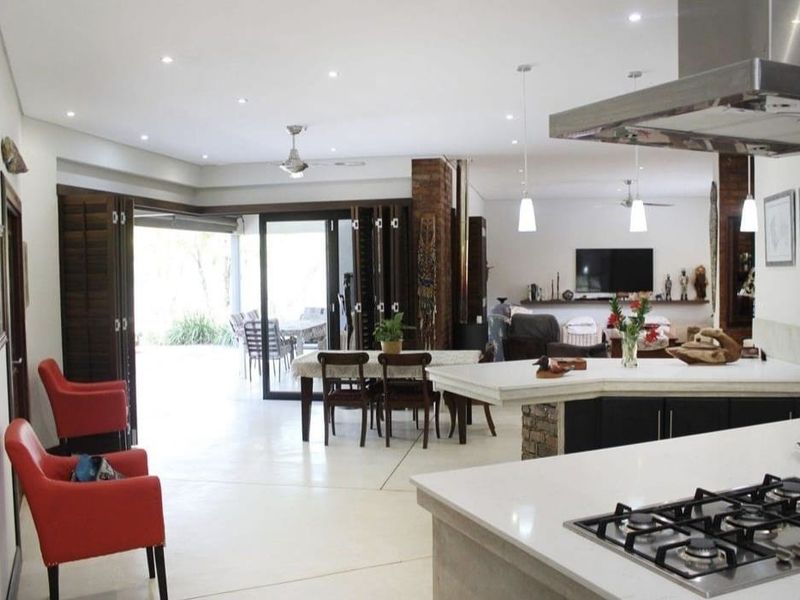 Spacious open-plan living area featuring a modern kitchen with stone countertops, gas hob, and seamless flow to the outdoor patio through stacking glass doors.