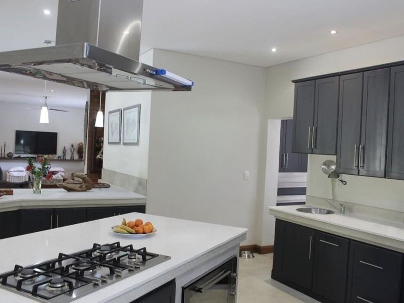 Modern open-plan kitchen featuring a large island with gas cooktop, sleek dark cabinetry, stone countertops, and integrated stainless steel extractor fan.