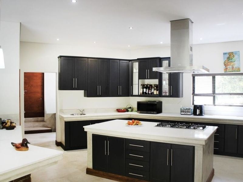 Modern kitchen featuring dark cabinetry, a large central island with a gas cooktop, stone countertops, and integrated stainless steel extractor fan.