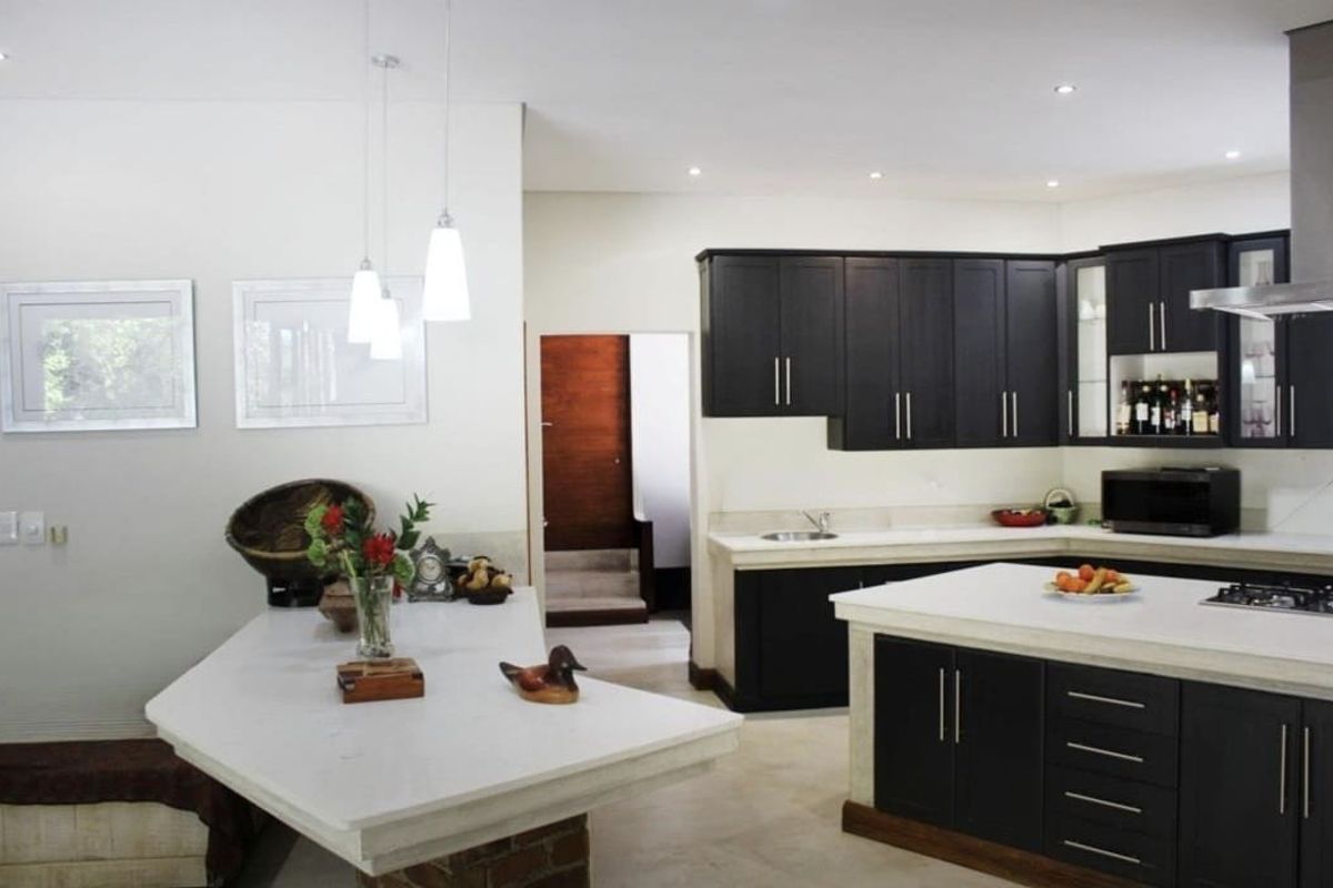 Modern kitchen featuring dark cabinetry, stone countertops, a central island, and integrated stainless steel appliances with recessed and pendant lighting.