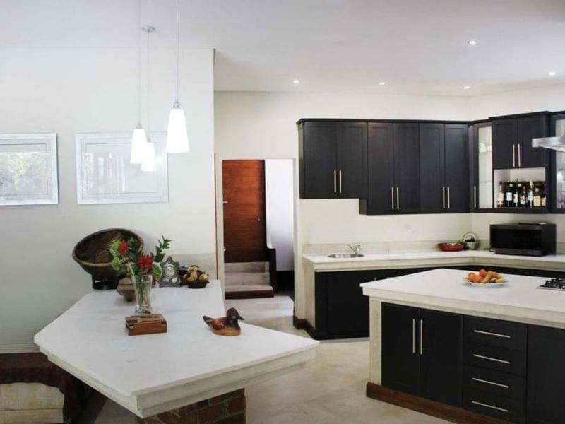 Modern kitchen featuring dark cabinetry, stone countertops, a central island, and integrated stainless steel appliances with recessed and pendant lighting.