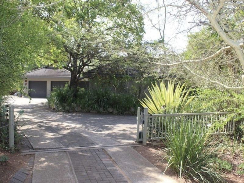 Front view of the property featuring a paved driveway, double garage, and gated entrance surrounded by established trees and landscaping.