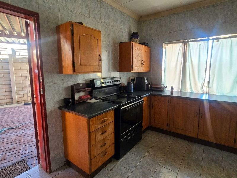 A dated kitchen featuring wooden cabinetry, laminate countertops, and a freestanding stove, with direct access to an outdoor paved patio area.