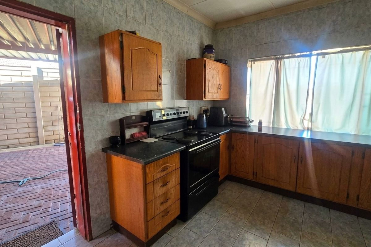 A dated kitchen featuring wooden cabinetry, laminate countertops, and a freestanding stove, with direct access to an outdoor paved patio area.