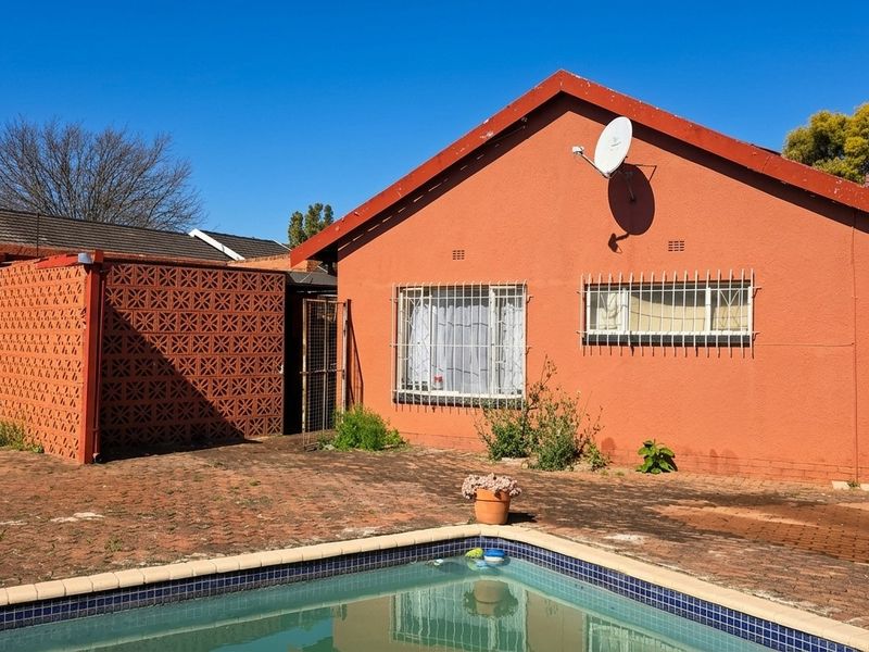 Rear exterior view of the house featuring a swimming pool, brick paved patio area, and security bars on the windows.