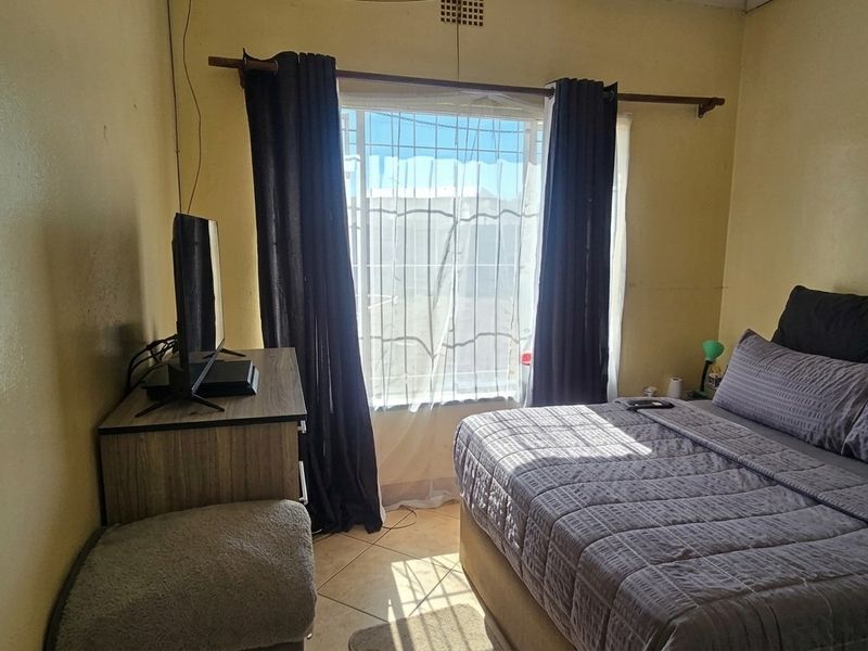 A bedroom featuring tiled flooring, a window with security bars, and a ceiling vent, requiring cosmetic updates to the wall finishes.