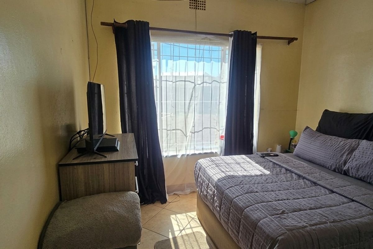 A bedroom featuring tiled flooring, a window with security bars, and a ceiling vent, requiring cosmetic updates to the wall finishes.