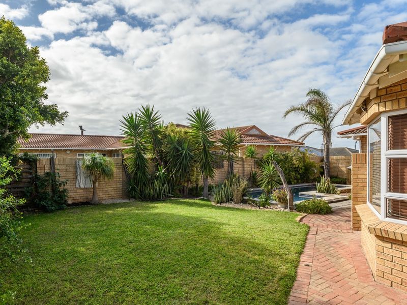 A well-maintained rear garden featuring a lawn, brick-paved pathway, and a swimming pool, bordered by a brick wall and established landscaping.