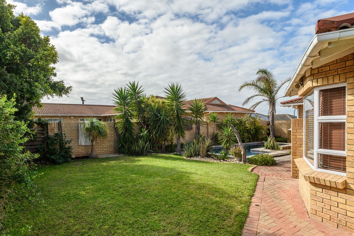 A well-maintained rear garden featuring a lawn, brick-paved pathway, and a swimming pool, bordered by a brick wall and established landscaping.