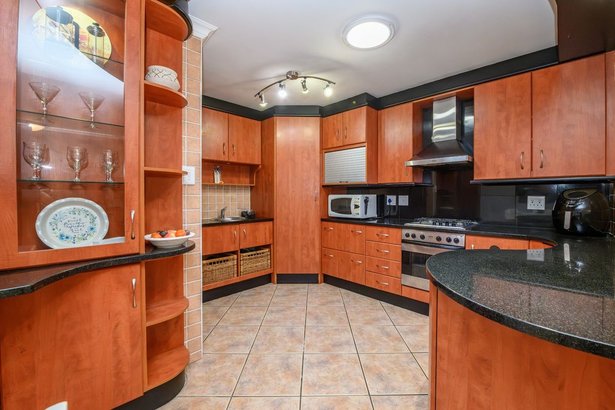 A functional kitchen featuring cherry wood cabinetry, granite countertops, a gas hob, and a stainless steel extractor fan with tiled flooring throughout.