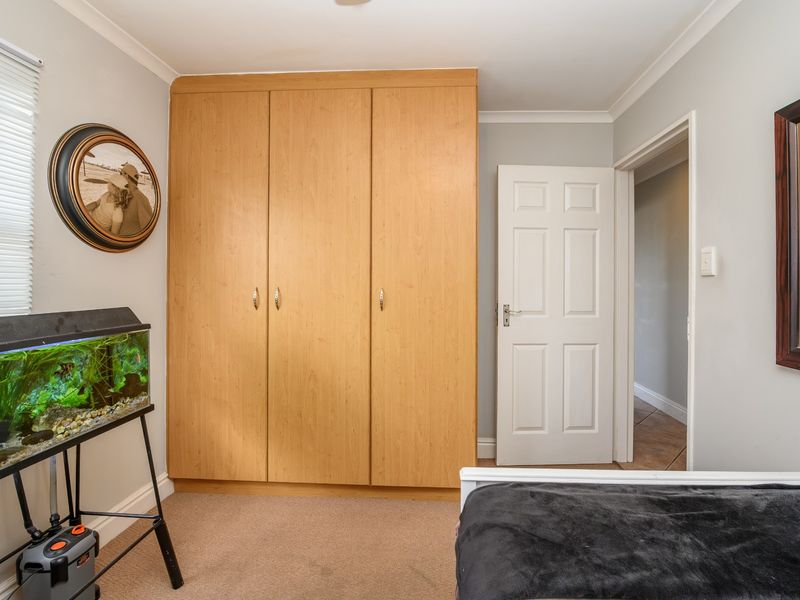 A well-maintained bedroom featuring neutral walls, carpet flooring, and a large built-in wooden wardrobe providing ample storage space.