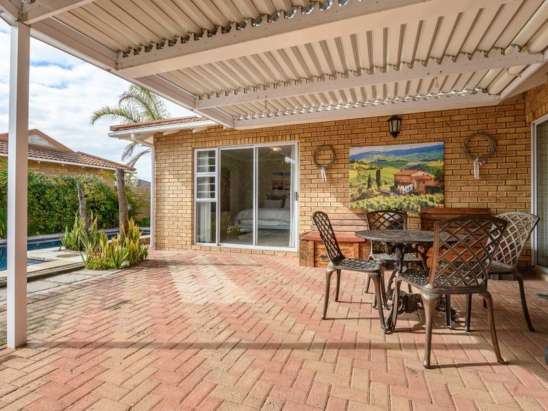 A covered brick-paved patio area featuring sliding glass door access to the interior and views of the adjacent swimming pool.