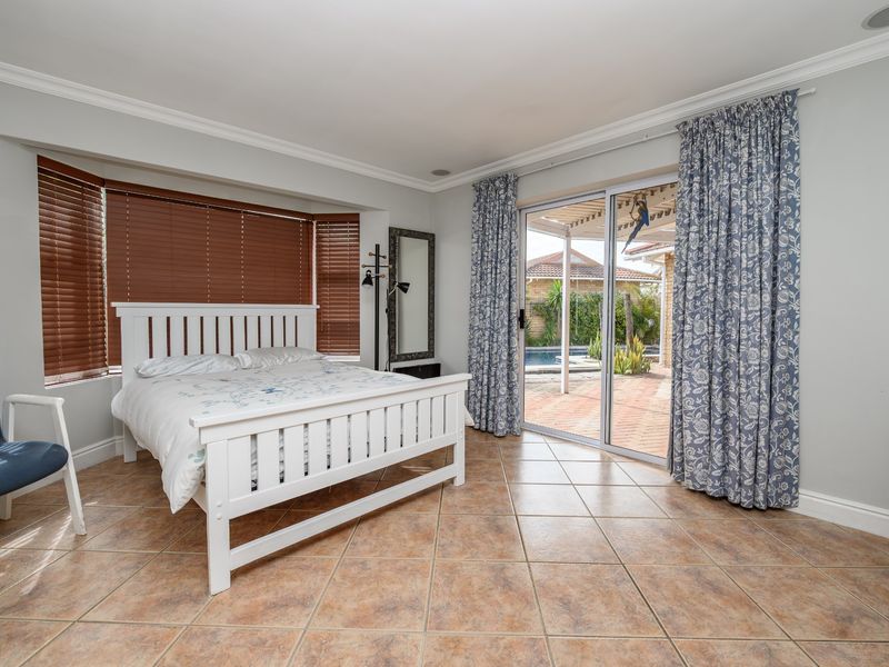 Spacious bedroom featuring ceramic tile flooring, a bay window with blinds, and sliding glass doors providing direct access to the outdoor patio and pool area.