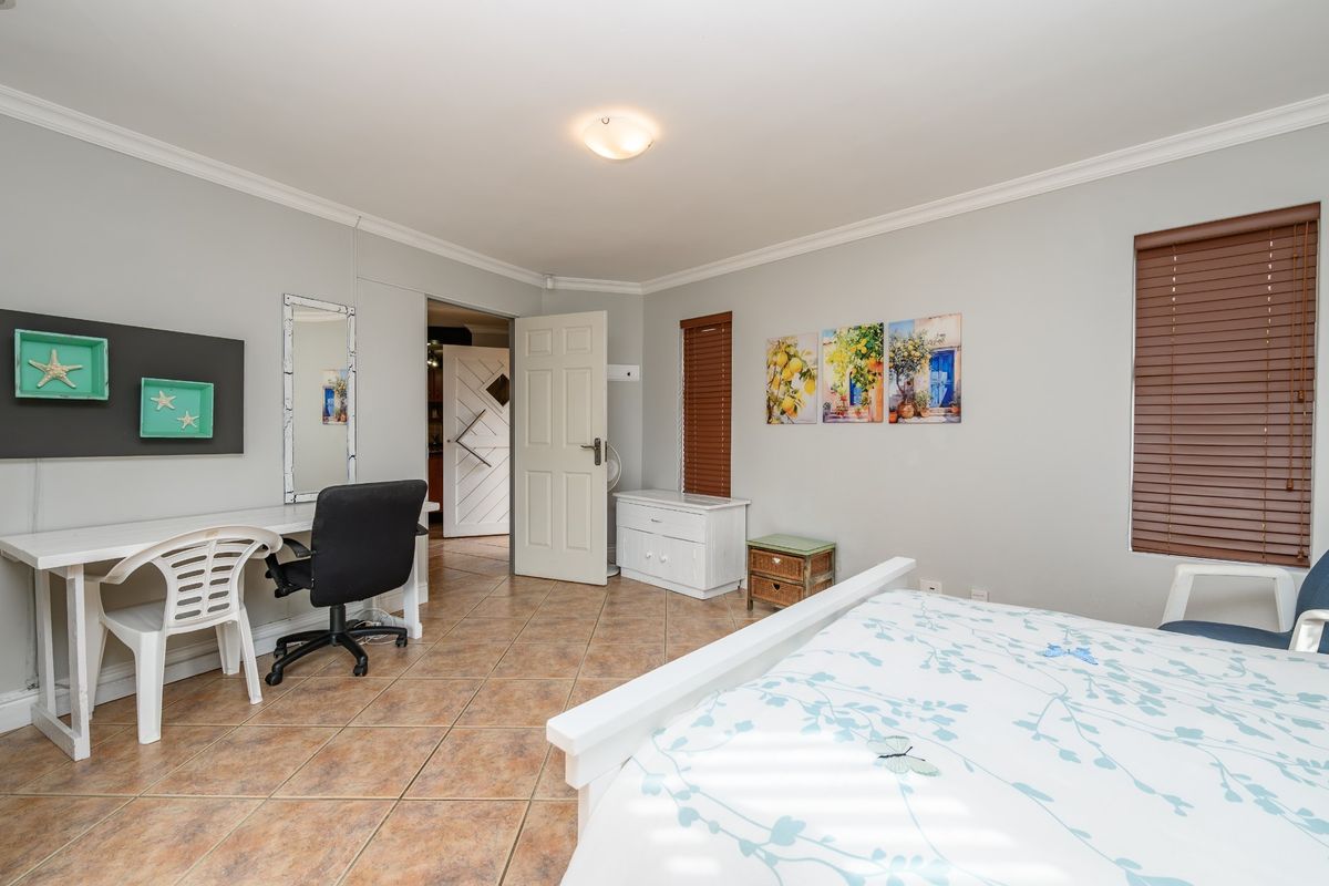 A well-maintained bedroom featuring neutral wall tones, tiled flooring, crown molding, and fitted venetian blinds, offering a clean and functional living space.