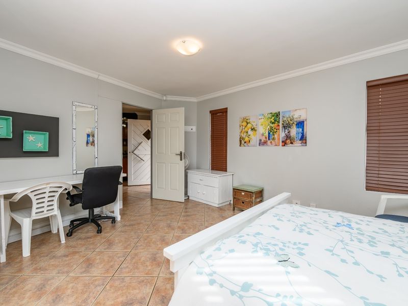 A well-maintained bedroom featuring neutral wall tones, tiled flooring, crown molding, and fitted venetian blinds, offering a clean and functional living space.