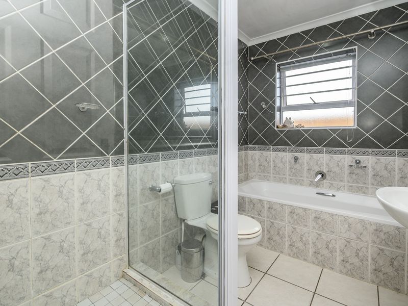 A functional bathroom featuring a shower enclosure, bathtub, pedestal basin, and toilet, finished with dual-tone wall tiling and a louvered window.