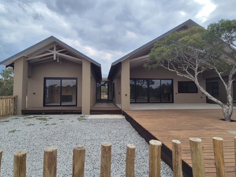 Modern rear exterior view featuring extensive timber decking, large sliding glass doors, and exposed roof trusses set within a natural landscape.