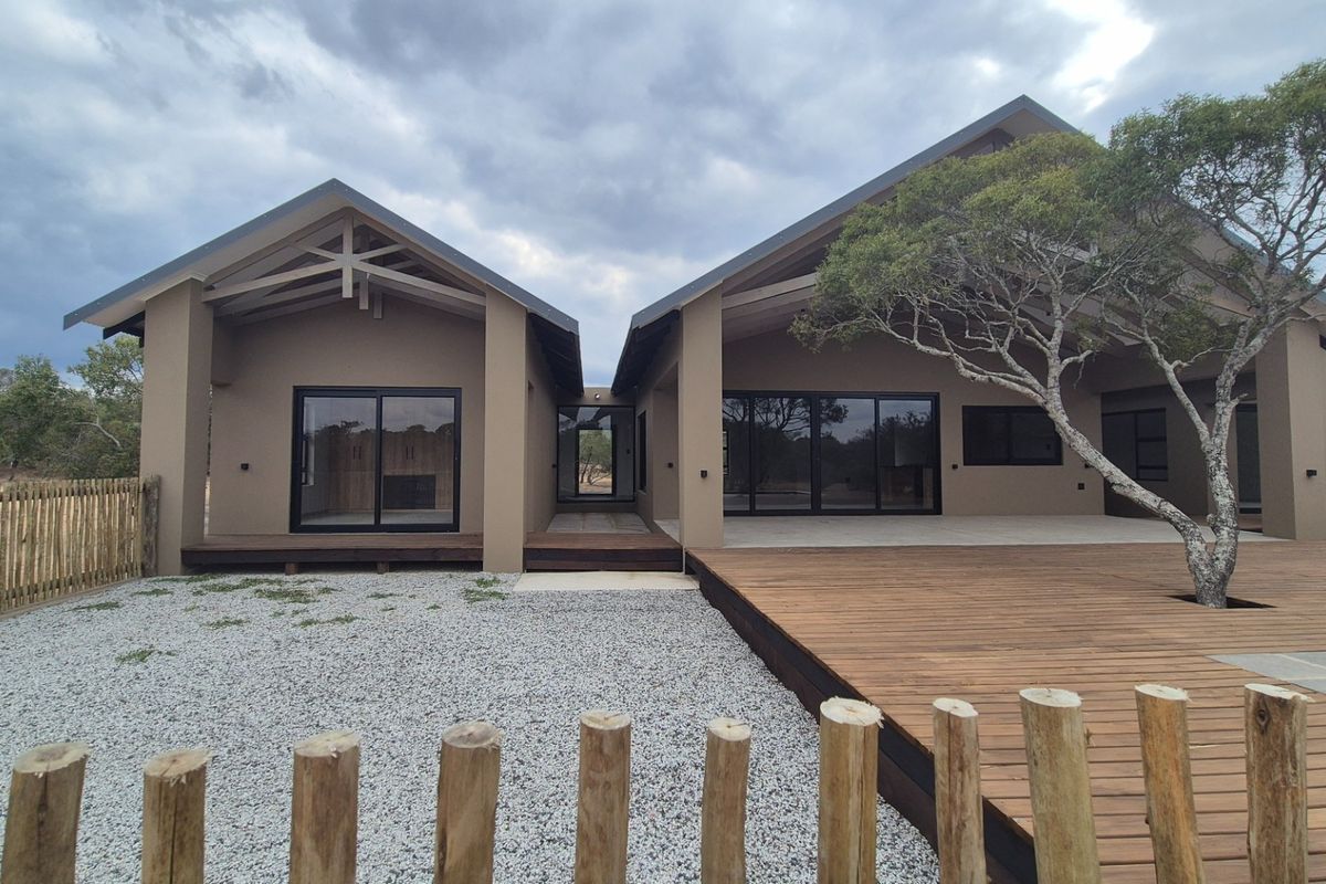 Modern rear exterior view featuring extensive timber decking, large sliding glass doors, and exposed roof trusses set within a natural landscape.