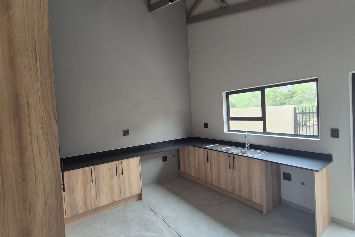 A modern, empty kitchen featuring light wood-look cabinetry, black countertops, a double sink, and polished concrete floors under exposed roof trusses.