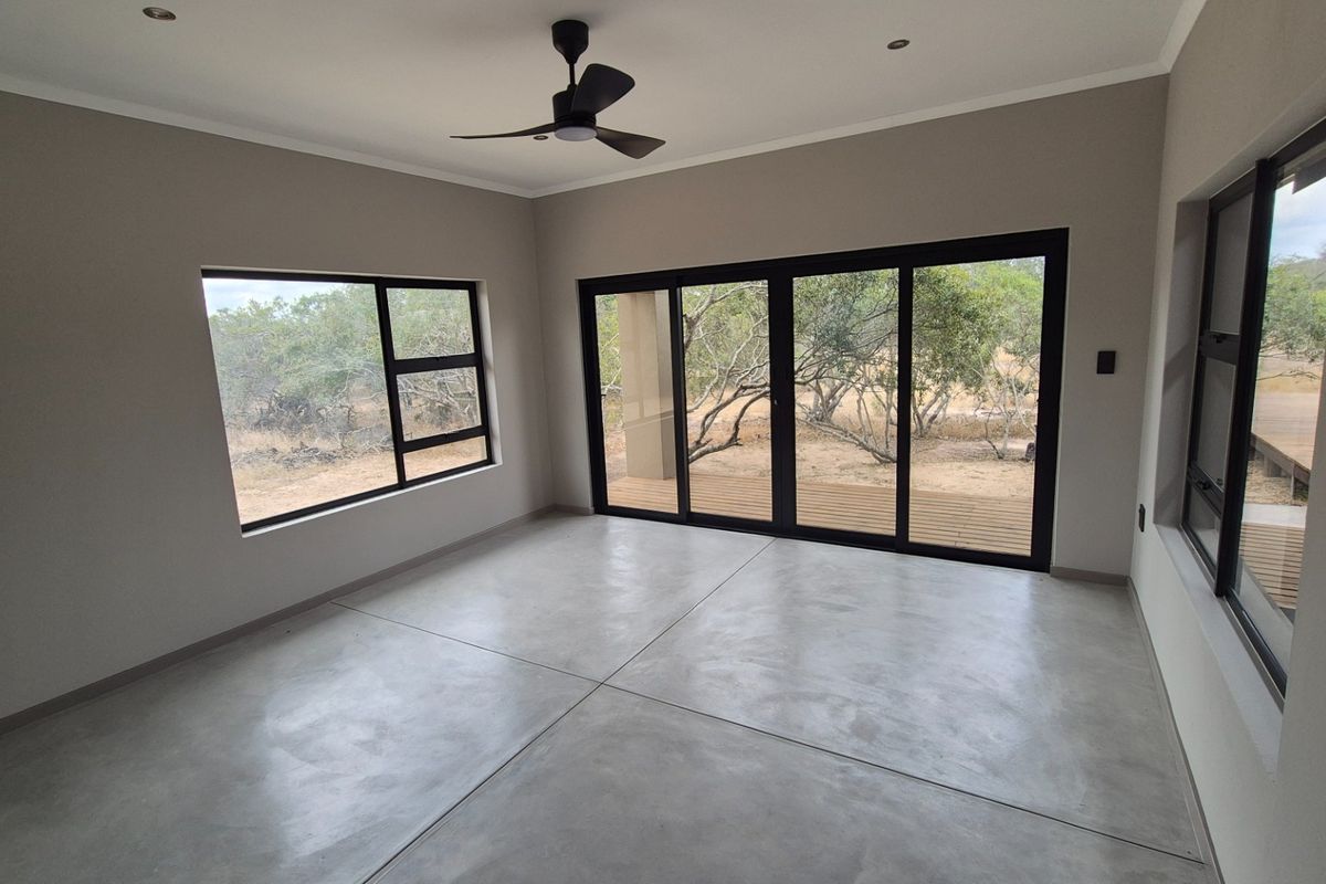 A bright, modern living room featuring polished concrete floors, large black aluminium sliding doors, and expansive windows with views of the surrounding natural landscape.