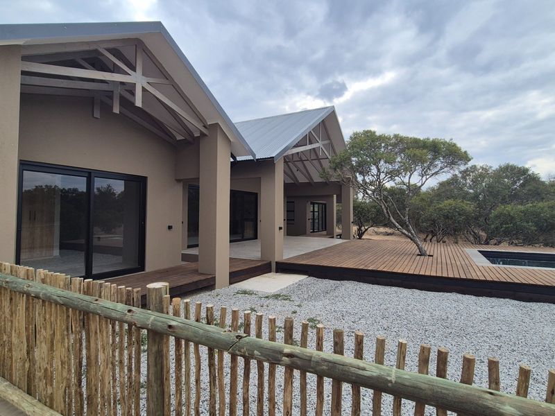 Rear view of a modern home featuring extensive timber decking, a swimming pool, and large sliding glass doors opening to the outdoor living area.