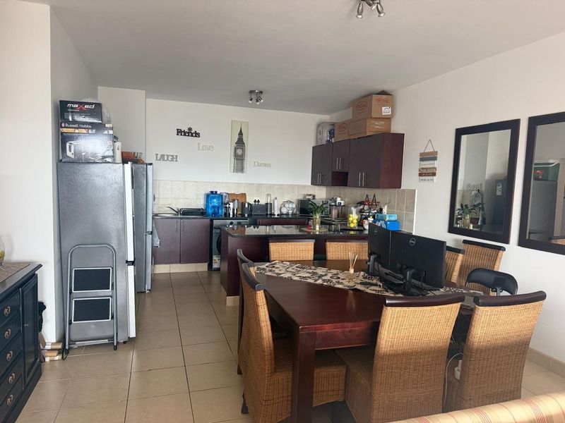 Open-plan living and dining area featuring a functional kitchen with built-in cabinetry, tiled backsplash, and a central island, finished with neutral floor tiles.