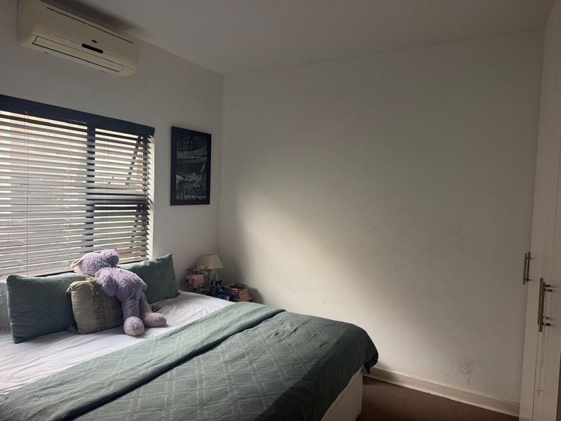 A bedroom featuring a split-system air conditioner, venetian blinds, and a built-in wardrobe with visible wall scuffing and staining.
