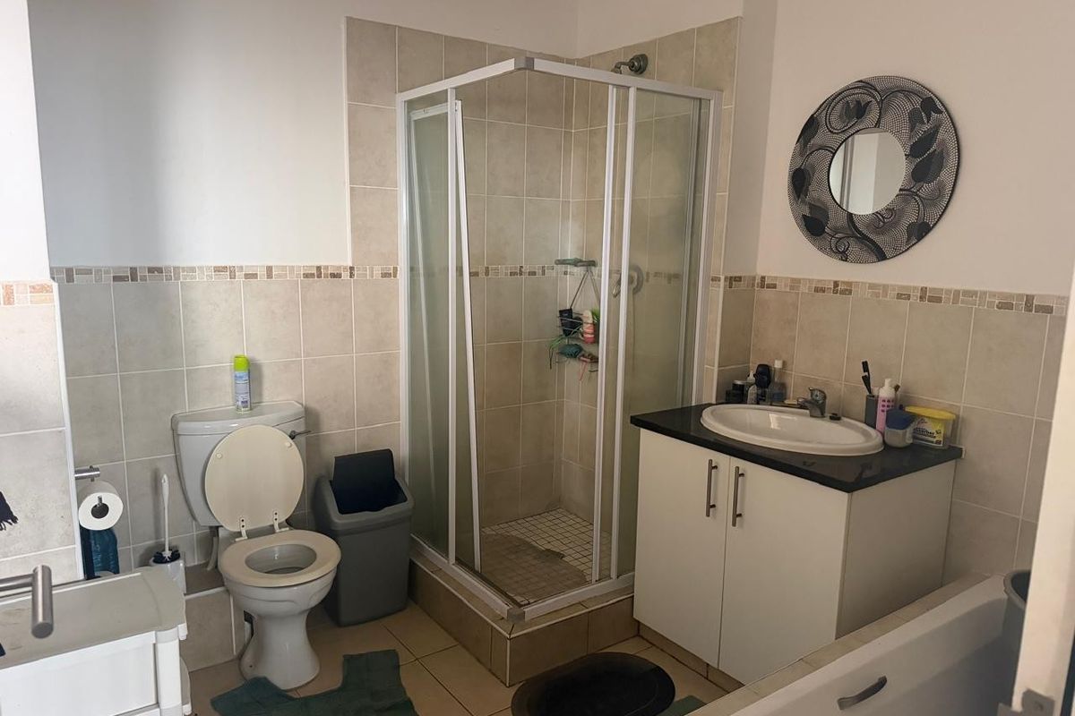A functional bathroom featuring a corner shower enclosure, vanity cabinet with basin, and toilet, finished with neutral wall and floor tiling.