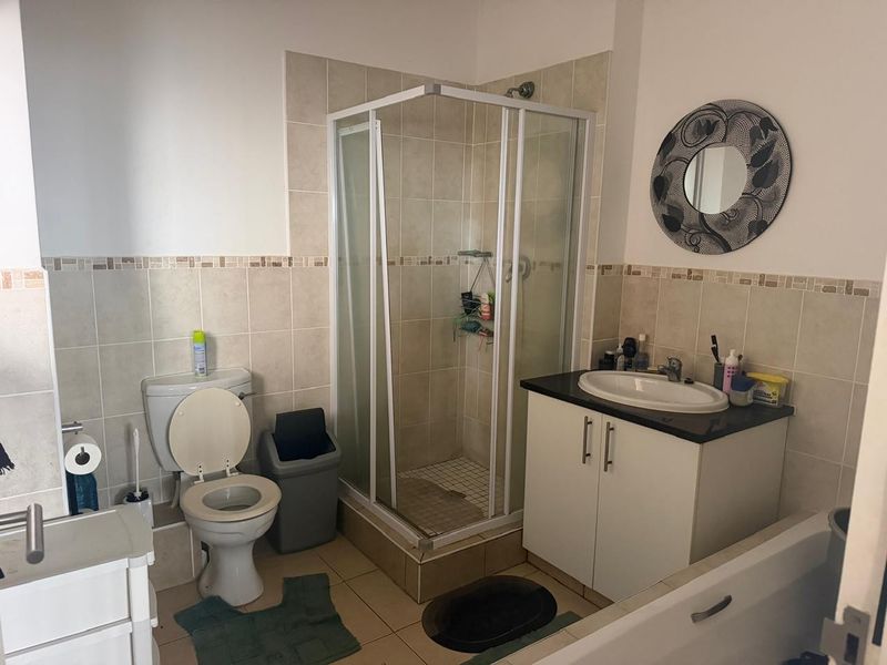 A functional bathroom featuring a corner shower enclosure, vanity cabinet with basin, and toilet, finished with neutral wall and floor tiling.
