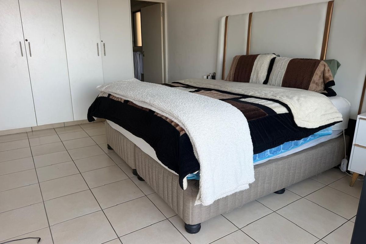 A bedroom featuring tiled flooring and built-in cupboards, with an adjacent doorway leading to an en-suite bathroom.