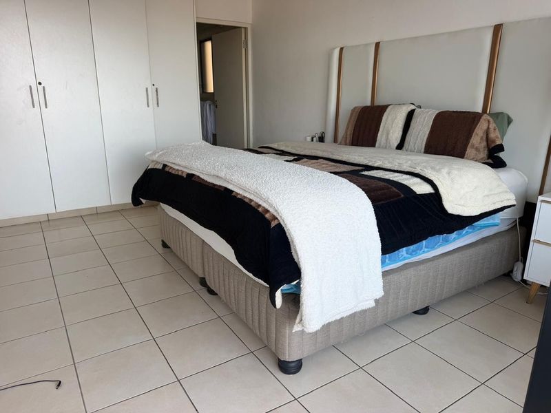 A bedroom featuring tiled flooring and built-in cupboards, with an adjacent doorway leading to an en-suite bathroom.