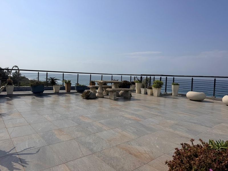 Spacious outdoor balcony featuring large format floor tiles and a metal safety railing, offering expansive ocean views.