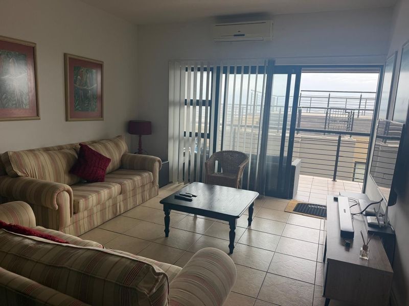 A living room featuring tiled flooring, a wall-mounted air conditioning unit, and large sliding glass doors providing access to an outdoor balcony area.