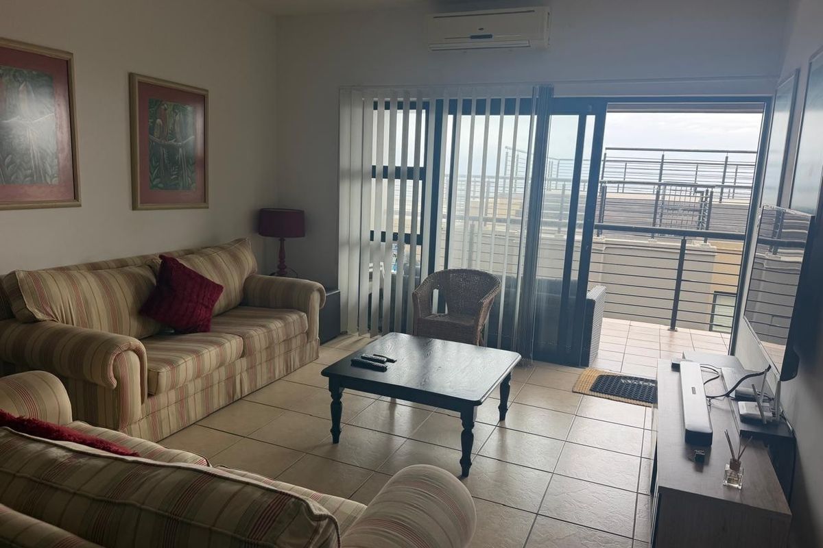 A living room featuring tiled flooring, a wall-mounted air conditioning unit, and large sliding glass doors providing access to an outdoor balcony area.