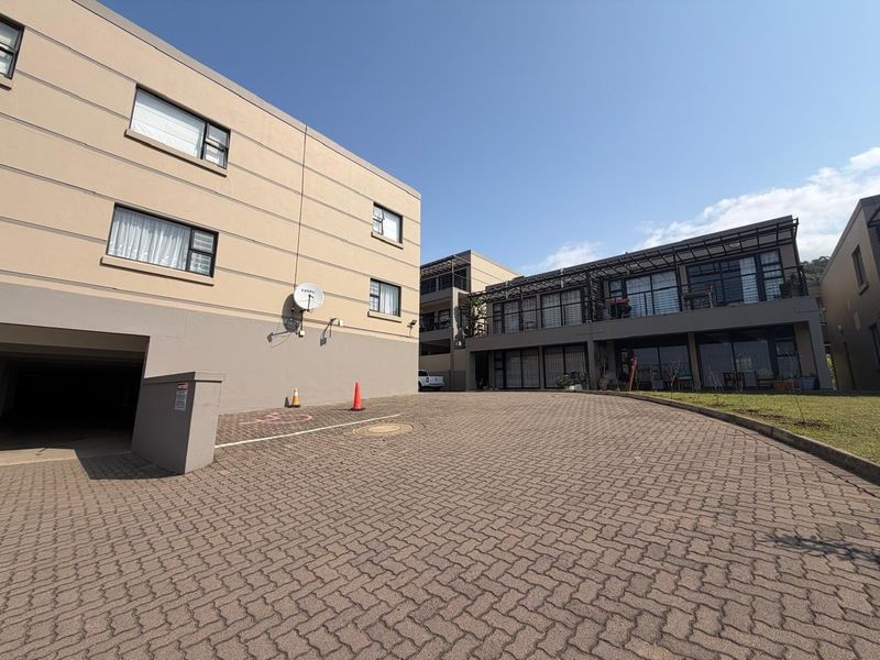 Exterior view of a modern apartment complex featuring a paved driveway, covered parking access, and multi-level units with balconies.
