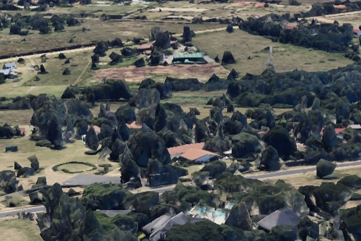 An aerial view of a residential area featuring open land, established trees, and surrounding road infrastructure.