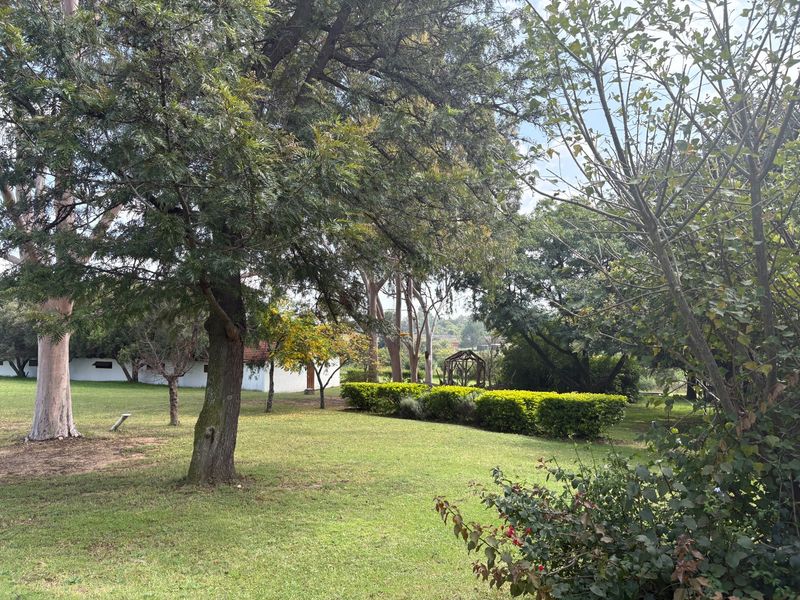 A spacious, well-maintained garden area featuring mature trees, manicured hedging, and expansive lawn space on the farm property.