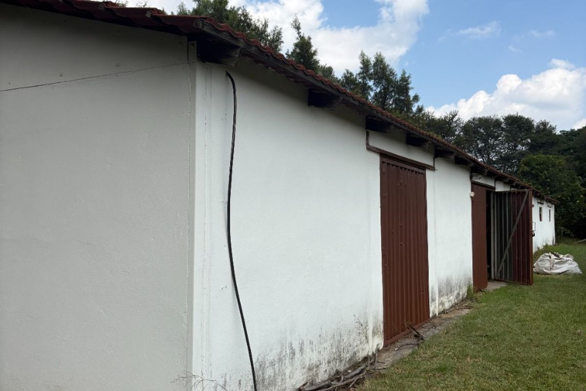 Rear view of a farm outbuilding featuring white plastered walls, metal doors, and a tiled roof, set on a grassy plot.