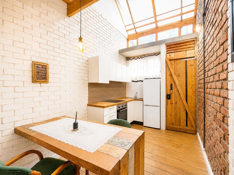 A charming open-plan kitchen and dining area featuring exposed brick walls, timber beams, a large skylight, and warm wooden flooring.