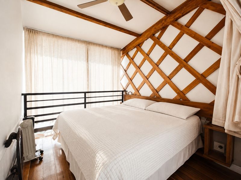 A cozy bedroom featuring unique wooden lattice wall detailing, exposed ceiling beams, hardwood flooring, and a metal balustrade overlooking the lower level.