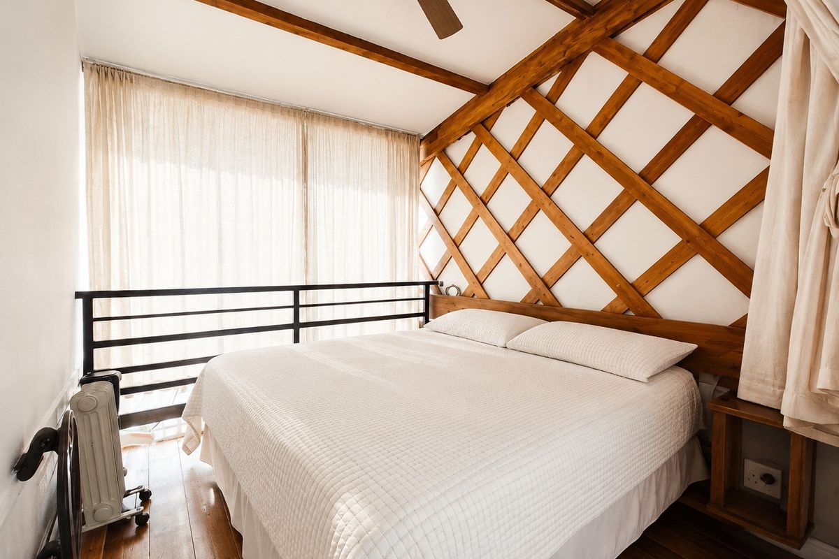 A cozy bedroom featuring unique wooden lattice wall detailing, exposed ceiling beams, hardwood flooring, and a metal balustrade overlooking the lower level.