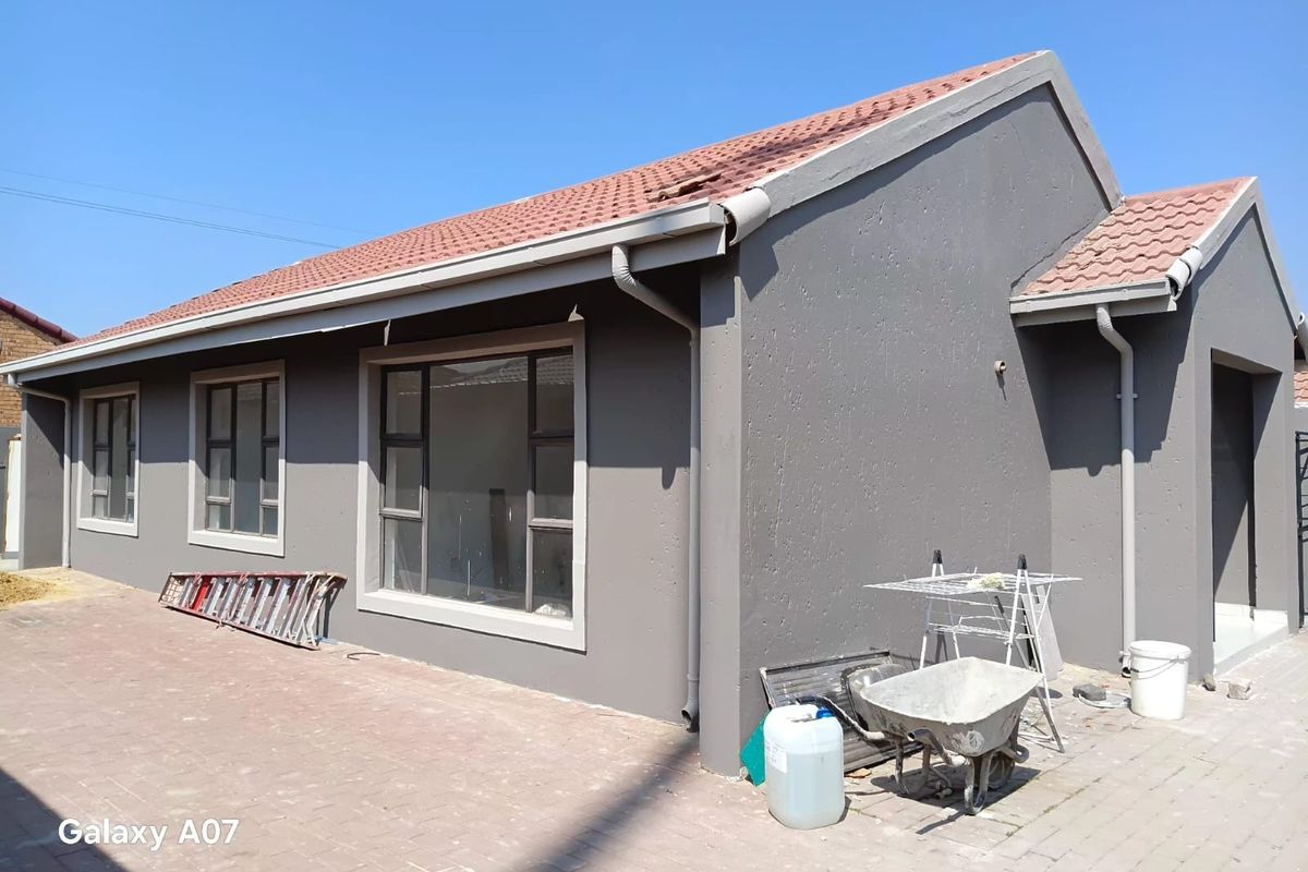 Rear exterior view of the house featuring a paved patio area, grey painted walls, and a tiled roof with some visible tile damage.