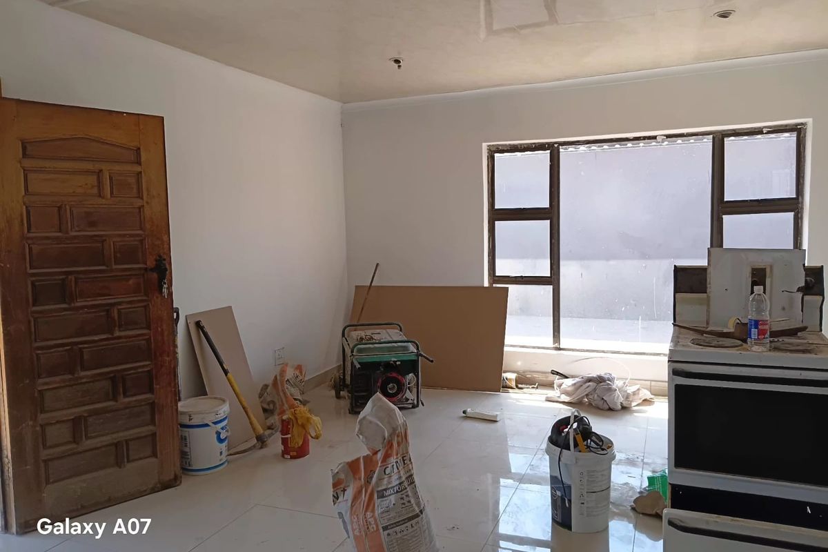 An unfinished kitchen space featuring tiled flooring, a freestanding stove, and a timber door, currently undergoing renovation or construction work.