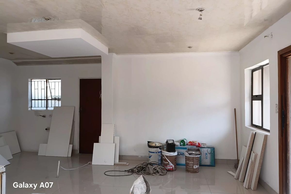 An empty living area featuring tiled floors, recessed ceiling details, and security bars on windows, currently undergoing renovation or finishing work.