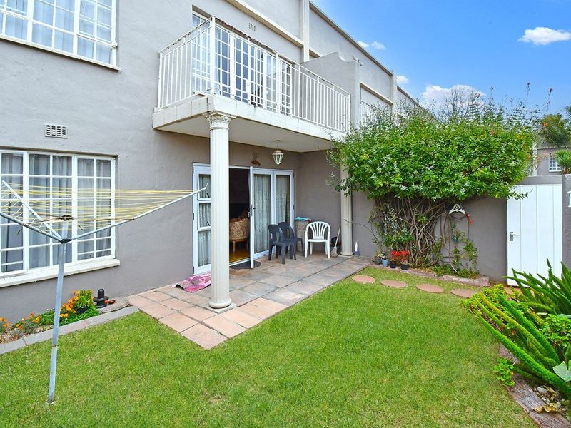 Rear view of the property featuring a private garden, paved patio area, and an upper-level balcony with wrought iron railings.