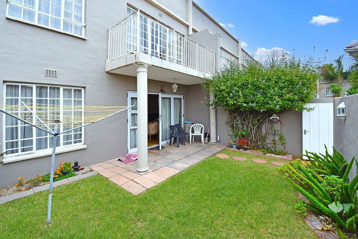 Rear view of the property featuring a private garden, paved patio area, and an upper-level balcony with wrought iron railings.