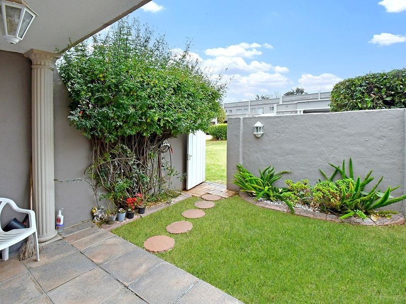 A private outdoor patio area featuring a covered space, paved flooring, a small lawn, and a boundary wall with access to the garden.