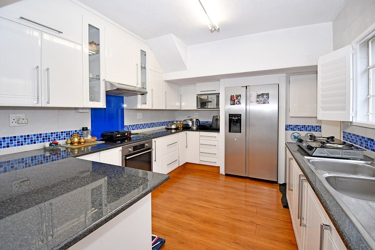 A functional kitchen featuring white cabinetry, granite countertops, a blue glass splashback, and integrated appliances including an oven and microwave.